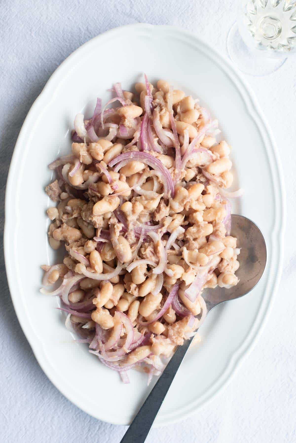 An overhead shot of cannellini beans, tuna and onion on a white platter.