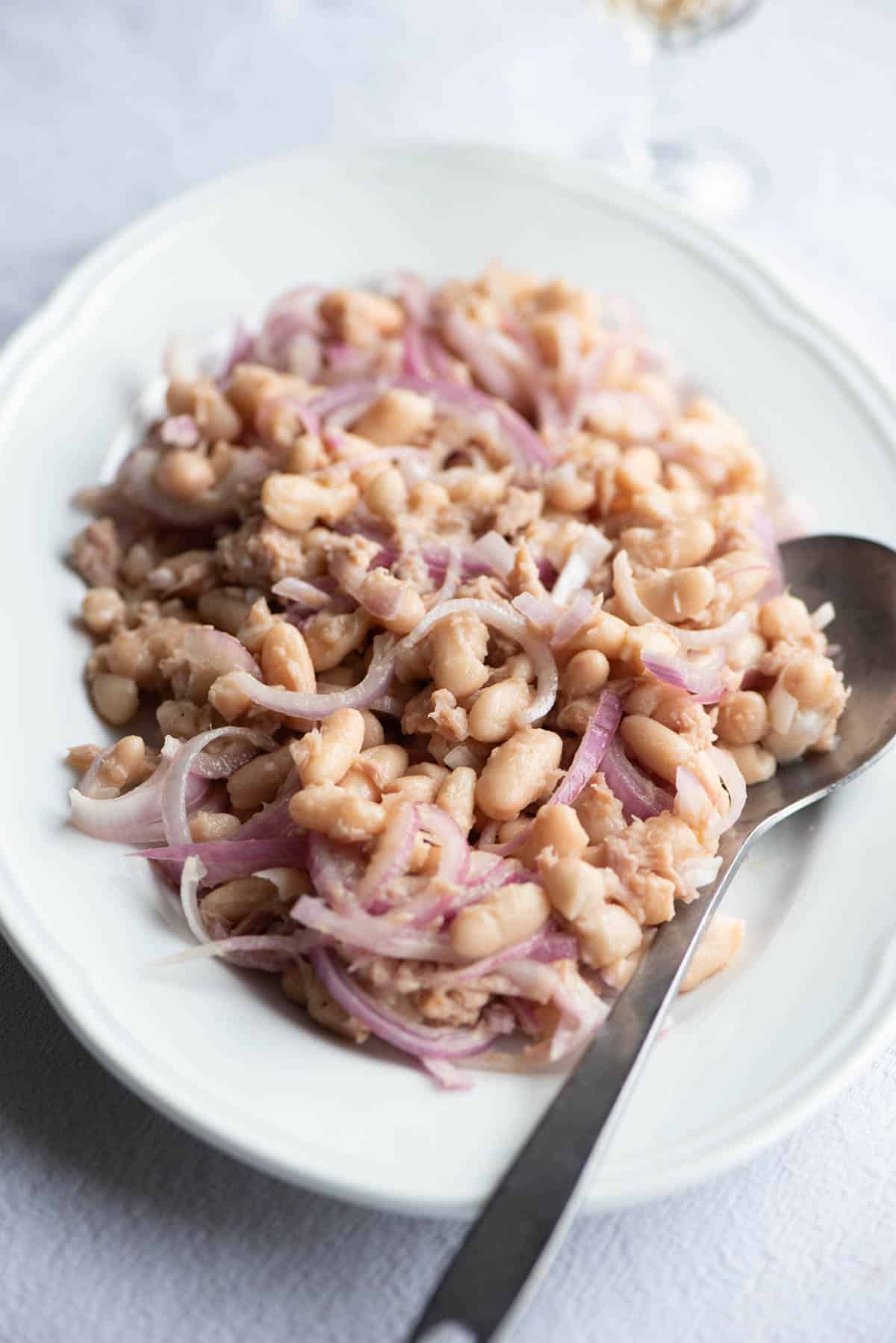 Cannellini beans, tuna and onion on a white plate with a serving spoon.