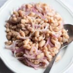 A cropped square image of a cannellini bean salad with tuna and onions on a white oval platter.