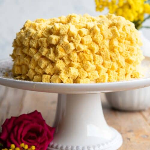 A mimosa cake on a cake stand with mimosa flowers in the background.