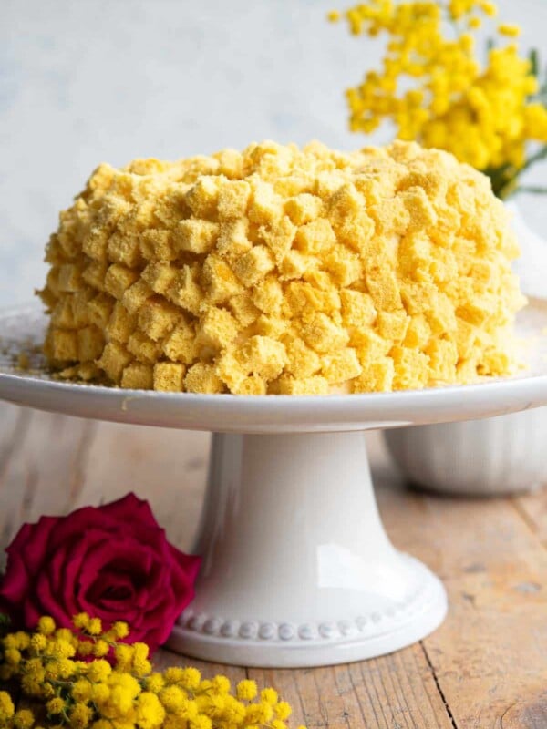 A mimosa cake on a cake stand with mimosa flowers in the background.
