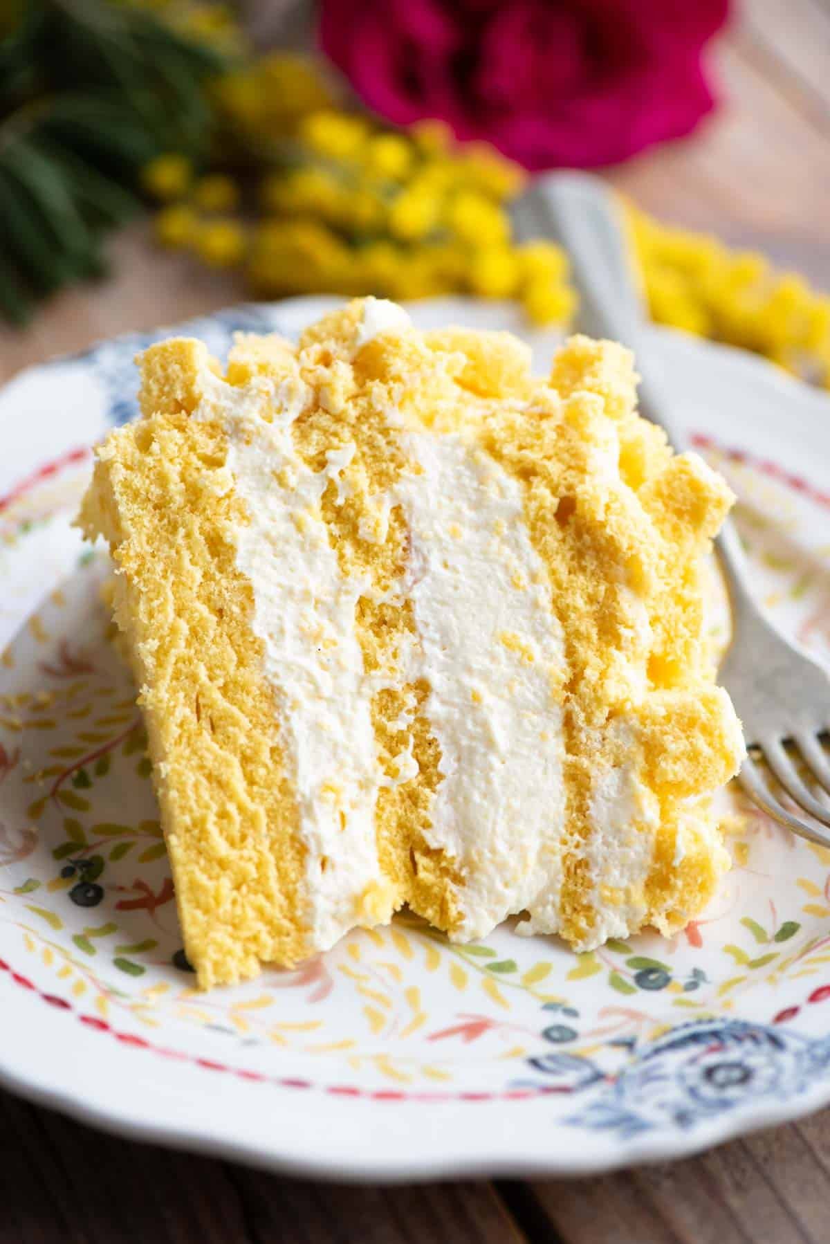 A slice of mimosa cake with three layers and filled with cream on a small plate.