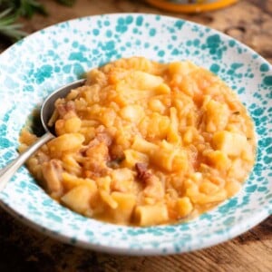 Pasta e Patate (potatoes) in a blue speckled bowl with a spoon sitting on a wooden surface.