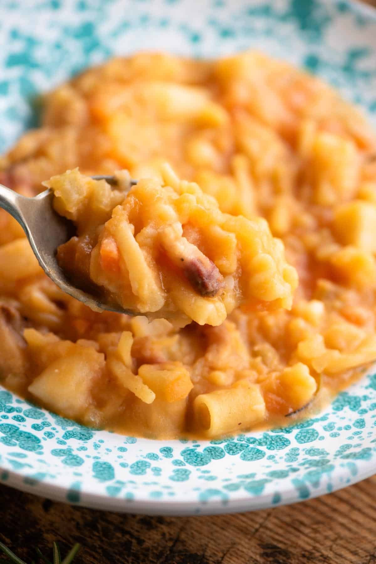 A close up of a spoonful of pasta and potatoes over a bowl.