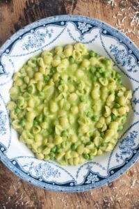 An overhead shot of Pasta and Piselli (peas) in a blue bowl sitting on a wooden surface.