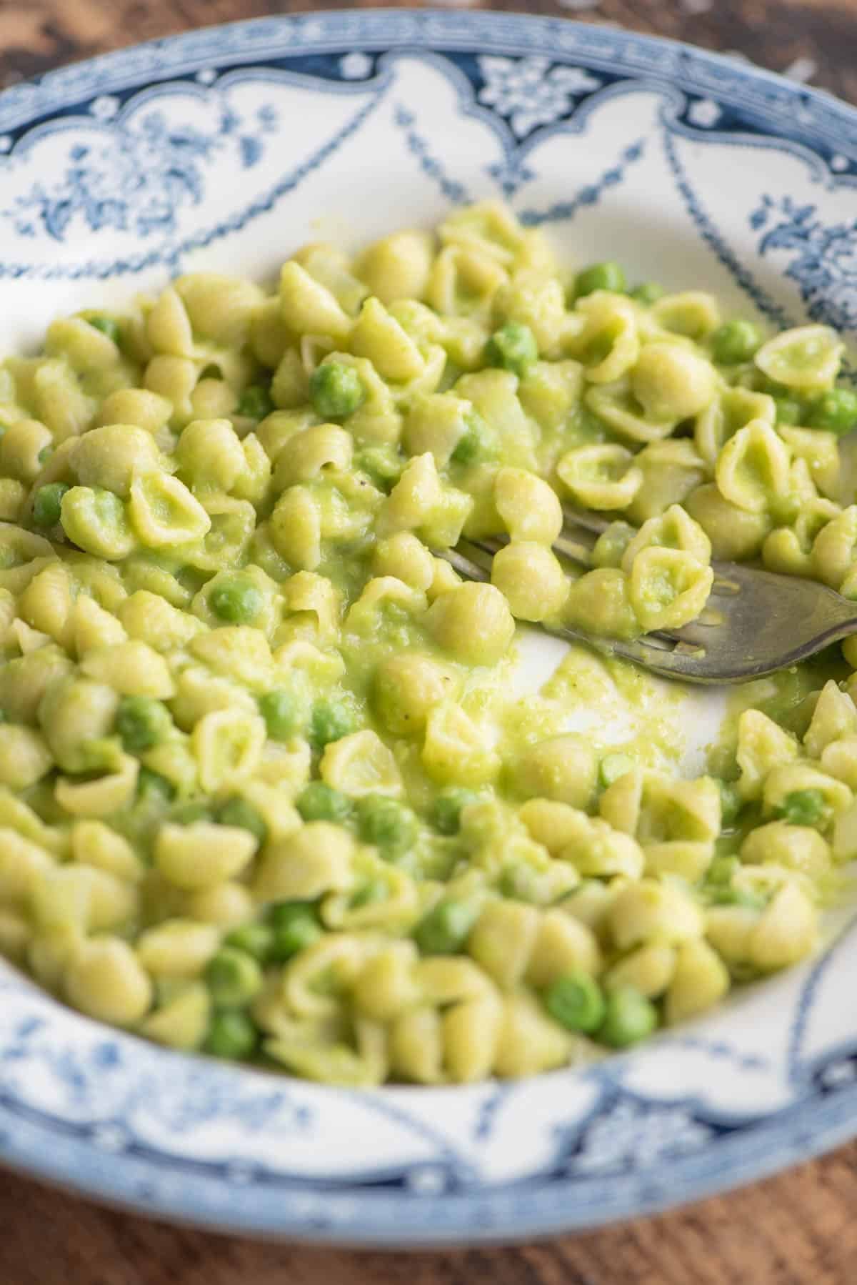A side shot of pasta and peas in a blue patterned bowl with a fork.