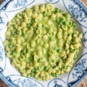 A cropped overhead shot of pasta and peas in a blue patterned bowl.