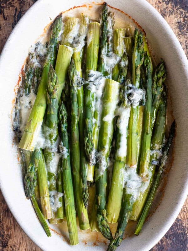An overhead shot of roasted asparagus in an oval baking dish topped with melted gorgonzola cheese.