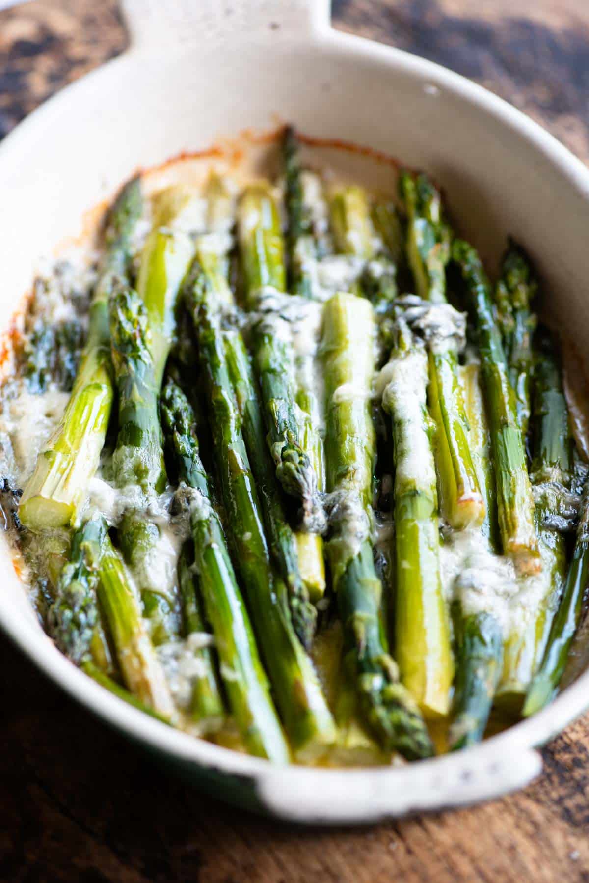 A side shot of roasted asparagus in an oval baking dish topped with gorgonzola.