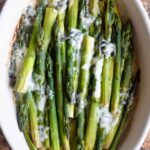A cropped square image of roasted asparagus in a baking dish topped with gorgonzola.