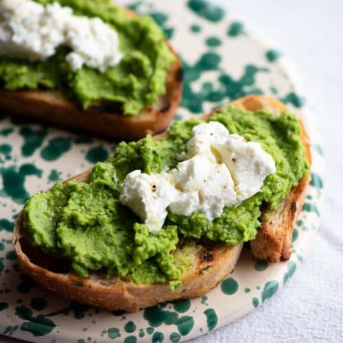 A close up of bruschetta topped with pea pesto and goat cheese on a ceramic serving board.