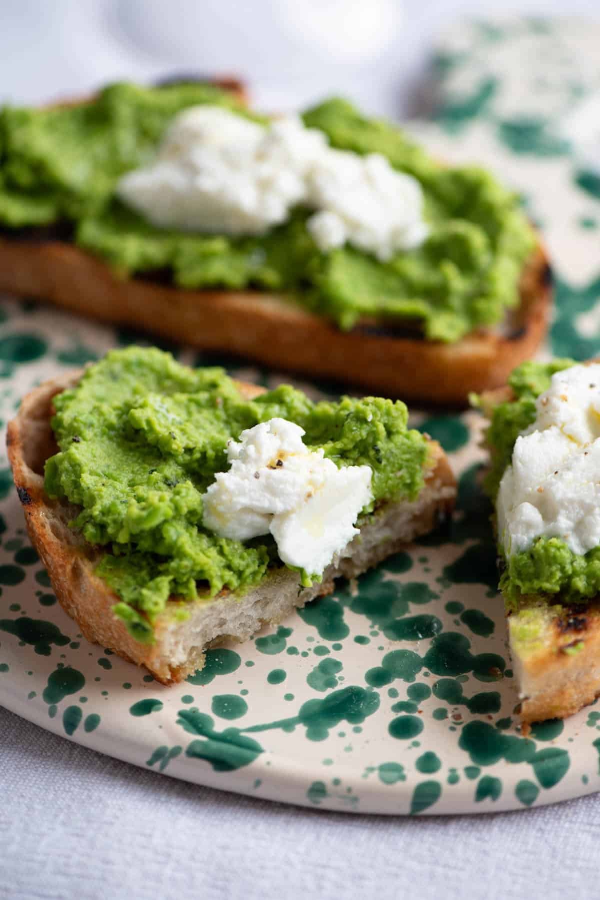 A close up of a piece of pea pesto bruschetta cut in half sitting on a ceramic serving board.