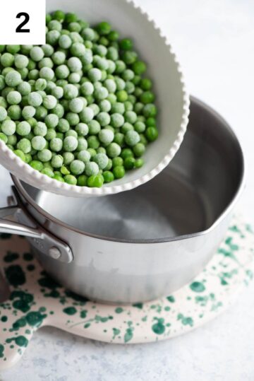 Frozen peas getting added to a small pot of boiling water.