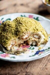 A close up of a piece of pistachio tiramisu on a plate sitting on a wooden table.