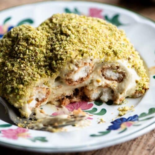 A close up of a piece of pistachio tiramisu on a plate sitting on a wooden table.