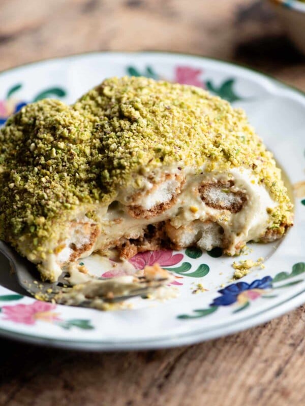 A close up of a piece of pistachio tiramisu on a plate sitting on a wooden table.