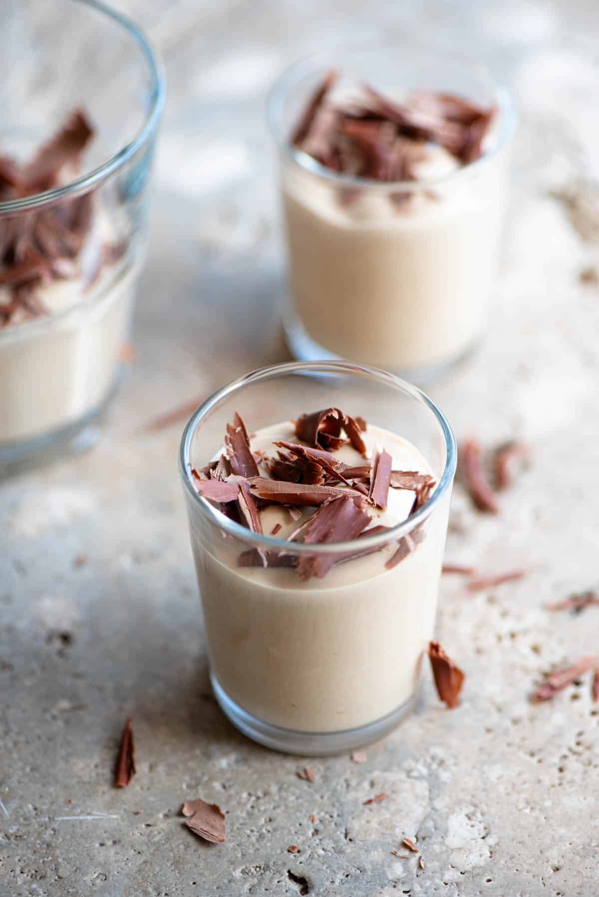 A close up of Ricotta al Caffe (ricotta and coffee) in small glasses topped with dark chocolate. The background is stone.