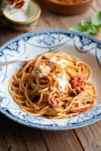 Roasted cherry tomato spaghetti in a blue bowl sitting on a wooden background.