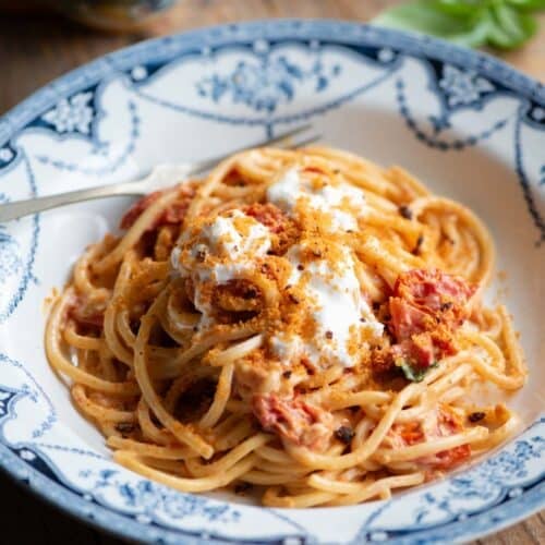 Roasted cherry tomato spaghetti in a blue bowl sitting on a wooden background.