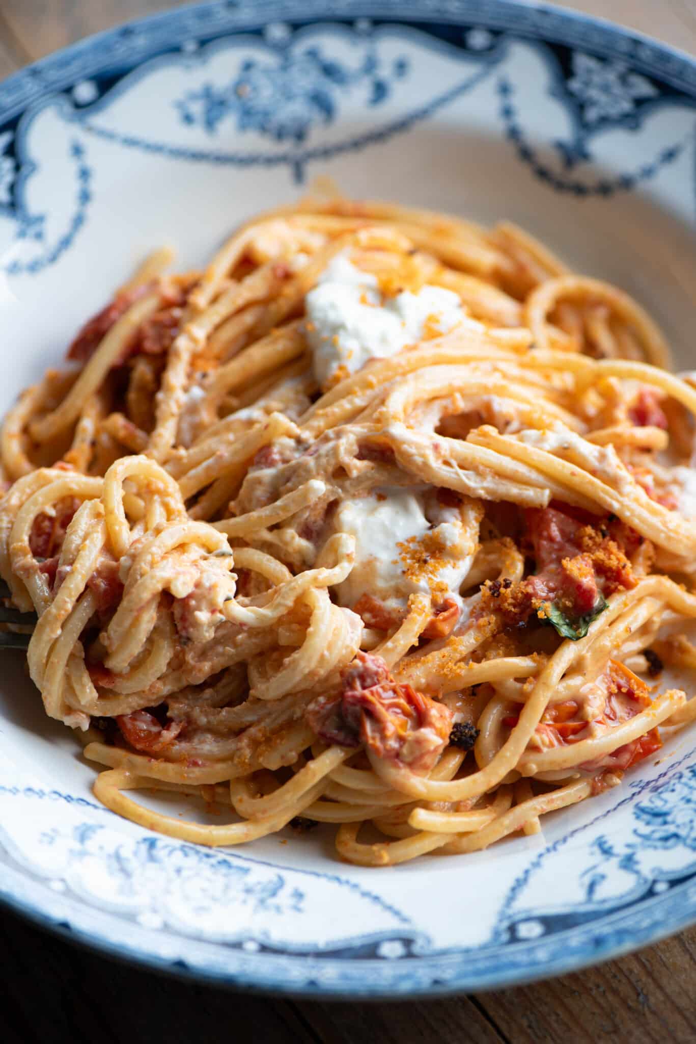 A close up of roasted cherry tomato spaghetti topped with burrata and Nduja breadcrumbs.