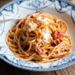 A cropped image of spaghetti in a roasted cherry tomato sauce in a blue bowl.