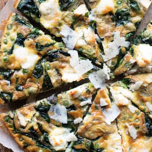 An overhead shot of a spinach and artichoke frittata cut into slices sitting on a wooden cutting board.