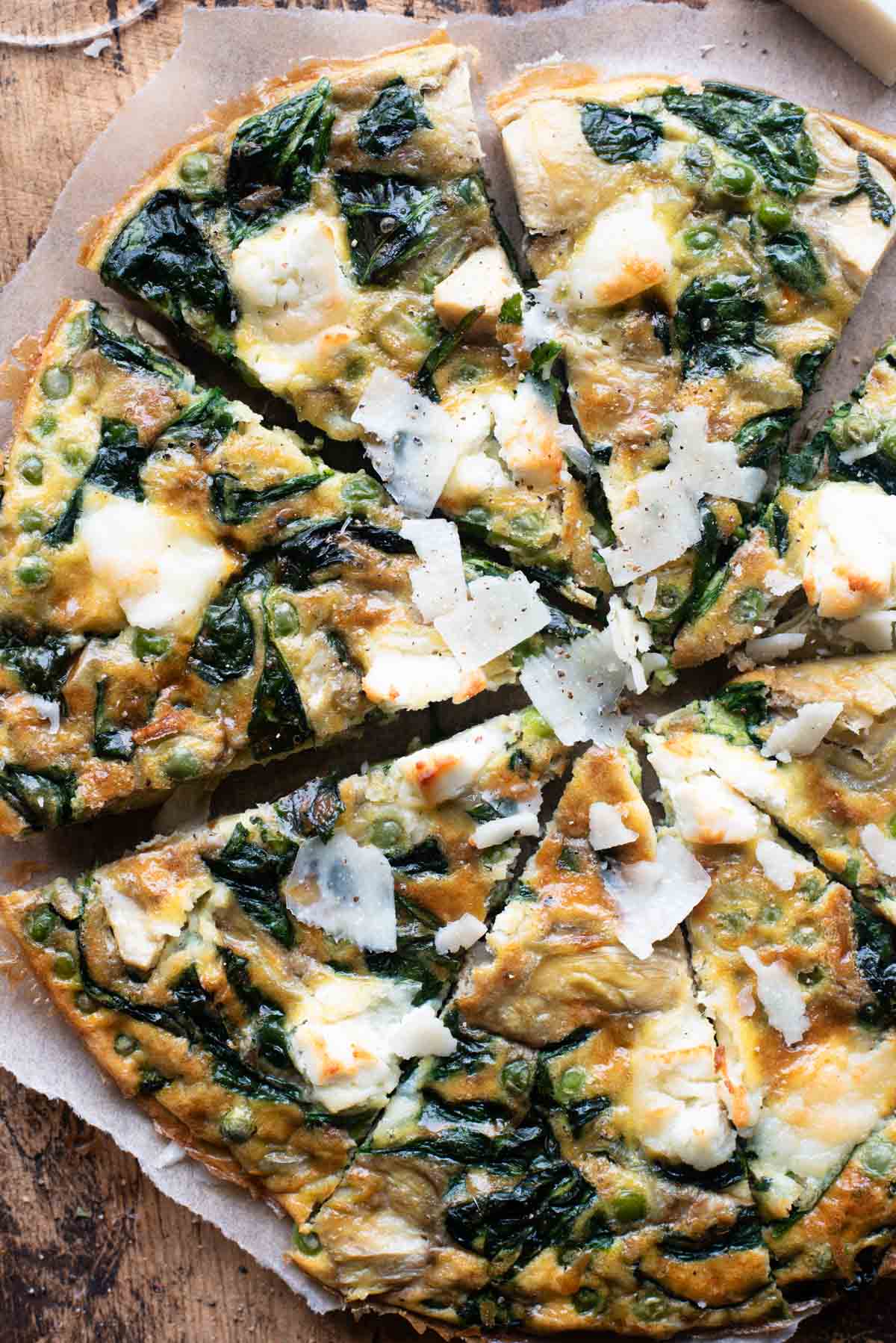 An overhead shot of a spinach and artichoke frittata cut into slices sitting on a wooden cutting board.