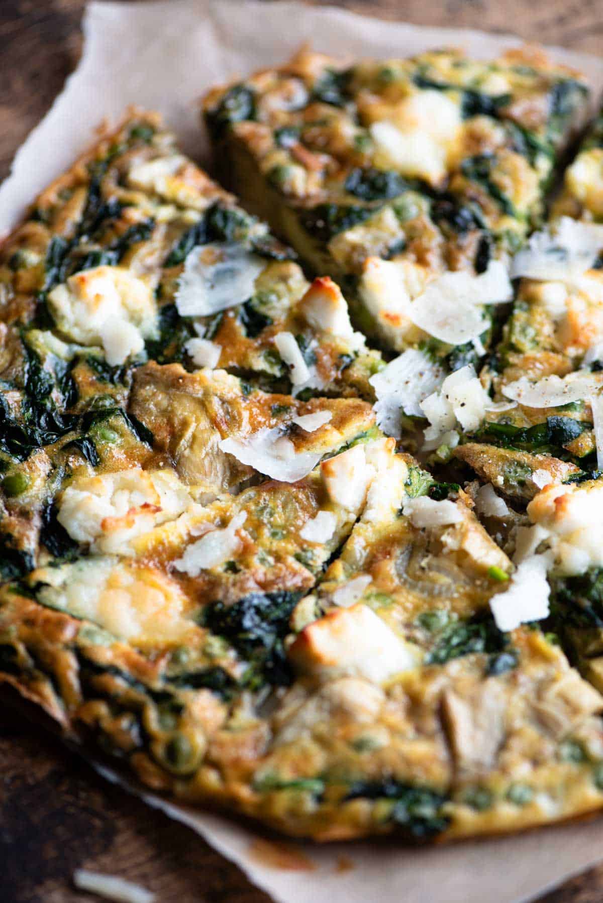 A close up of a spinach and artichoke frittata topped with goat's cheese cut into slices.