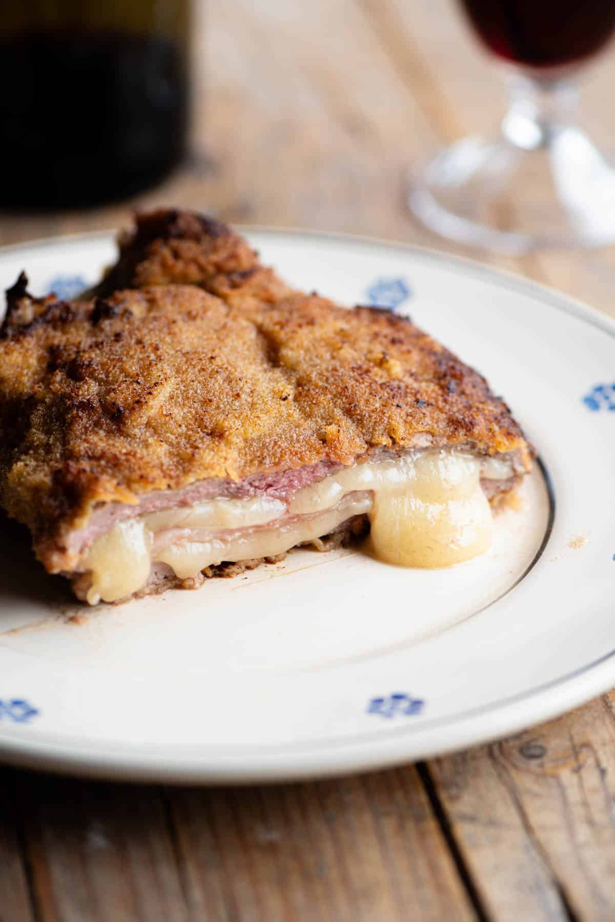 An Italian breaded veal chop (Cosoletta Valdostana) cut in half showing ham and cheese inside, oozing out.