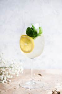 A Hugo spritz cocktail on a light coloured worktop with lemon and mint.