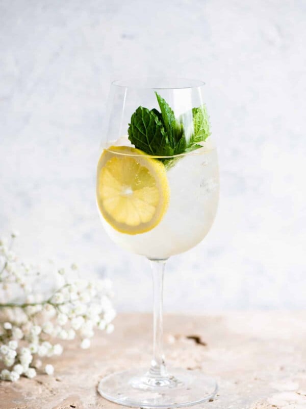 A Hugo spritz cocktail on a light coloured worktop with lemon and mint.