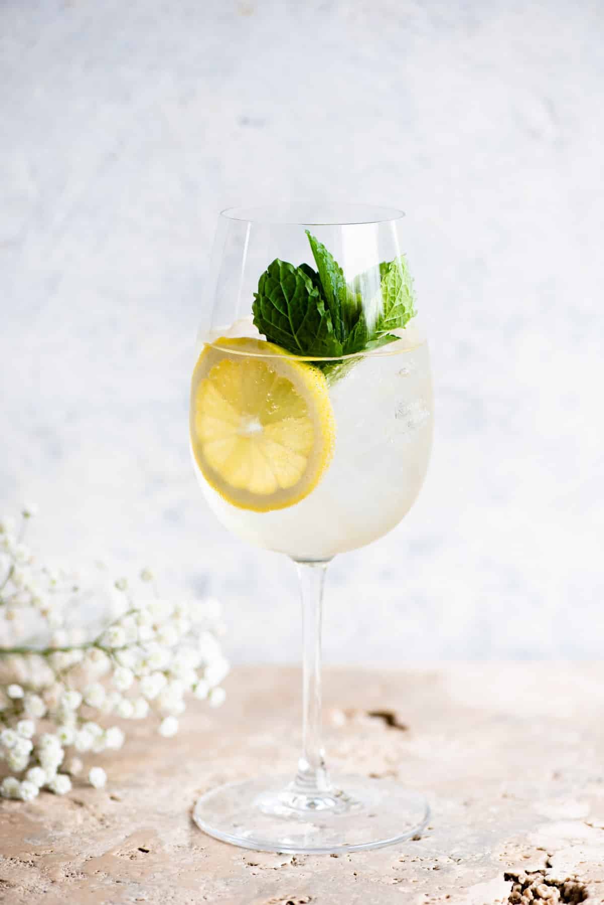 A hugo spritz cocktail garnished with lemon and mint.