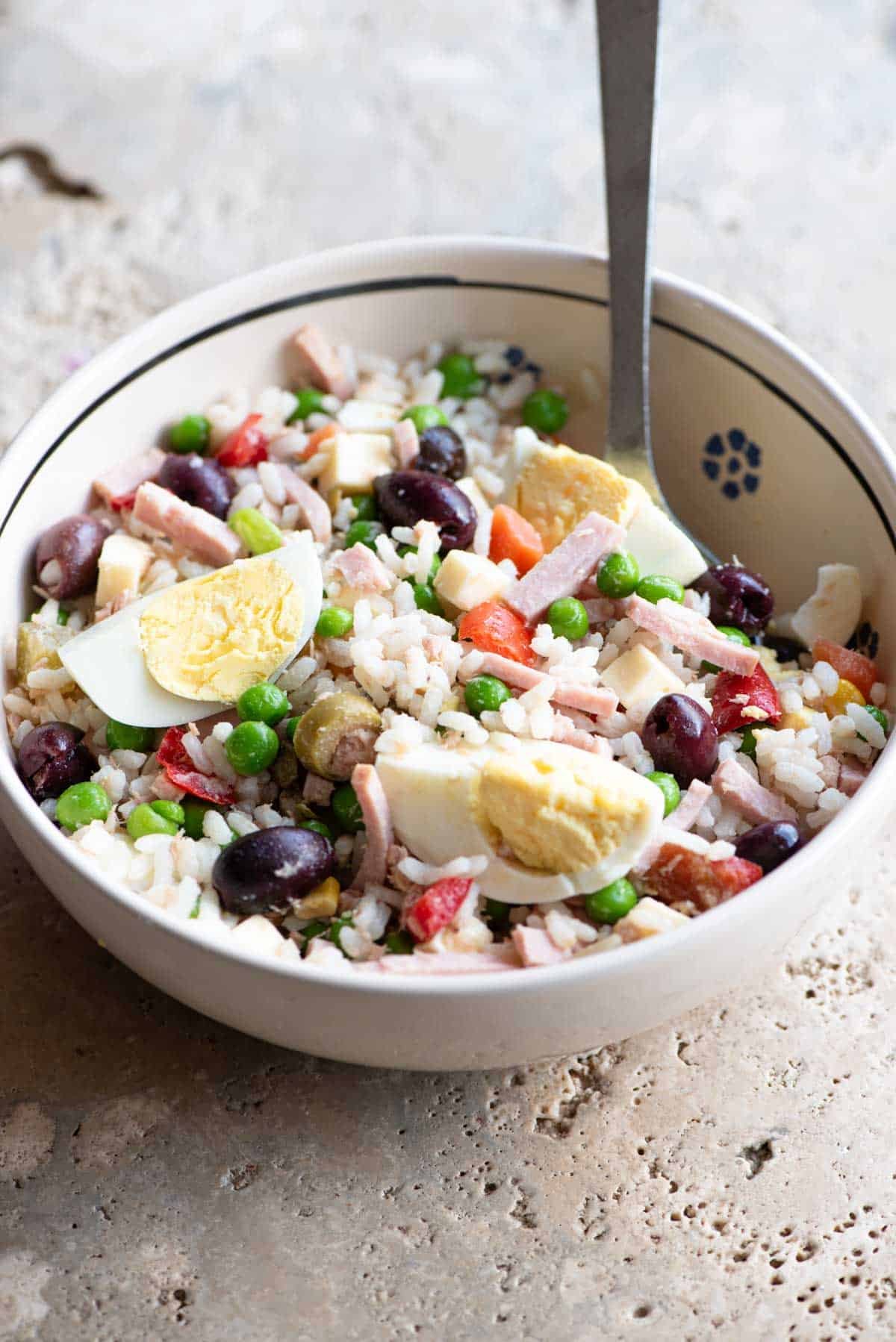 A traditional Italian rice salad in a bowl sitting on a rustic stone work top.