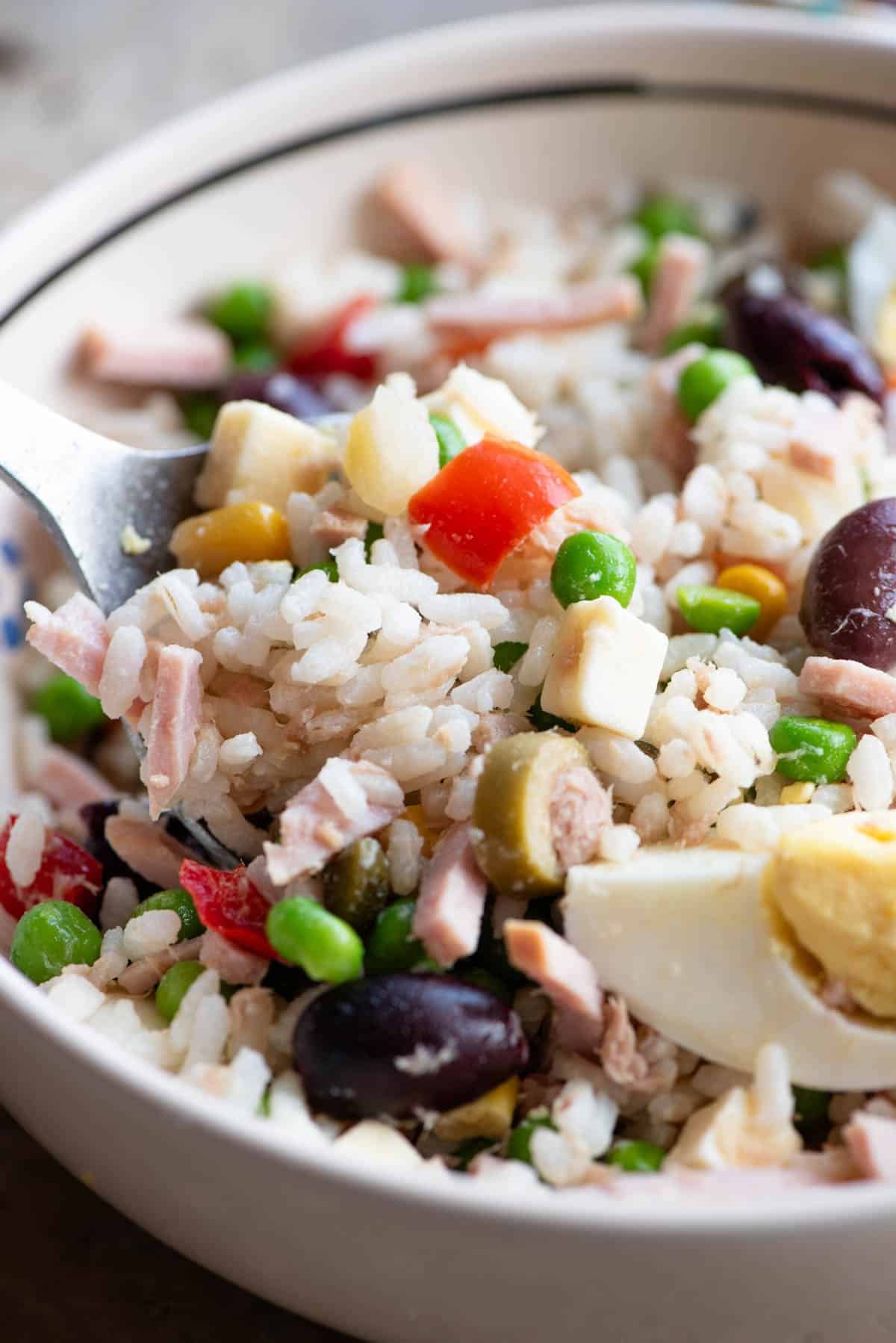 A close up of an Italian rice salad in a bowl with mixed vegetables, ham, tuna and hard-boiled eggs.
