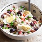 A cropped square image of an Italian rice salad in a bowl topped with eggs.