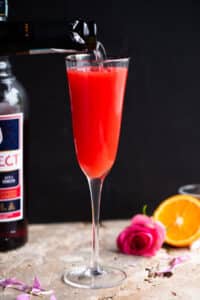 A select mimosa in a flute glass with prosecco getting poured in.