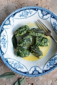 An overhead shot of Strangolapreti (Italian bread dumplings) on a blue and white plate sitting on a stone work surface.