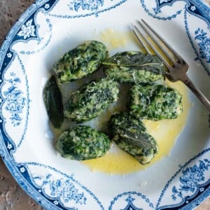 An overhead shot of Strangolapreti (Italian bread dumplings) on a blue and white plate sitting on a stone work surface.