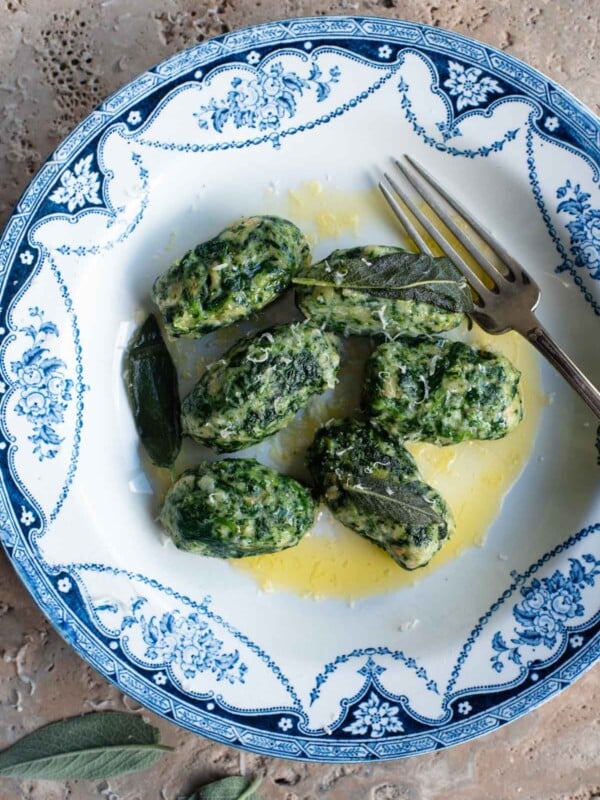 An overhead shot of Strangolapreti (Italian bread dumplings) on a blue and white plate sitting on a stone work surface.