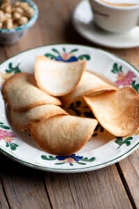 Tegole Valdostane cookies on a plate with a cappuccino at the side.