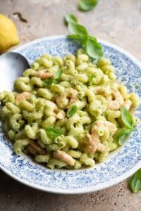 Zucchini shrimp pasta salad in a blue and white bowl topped with basil leaves.