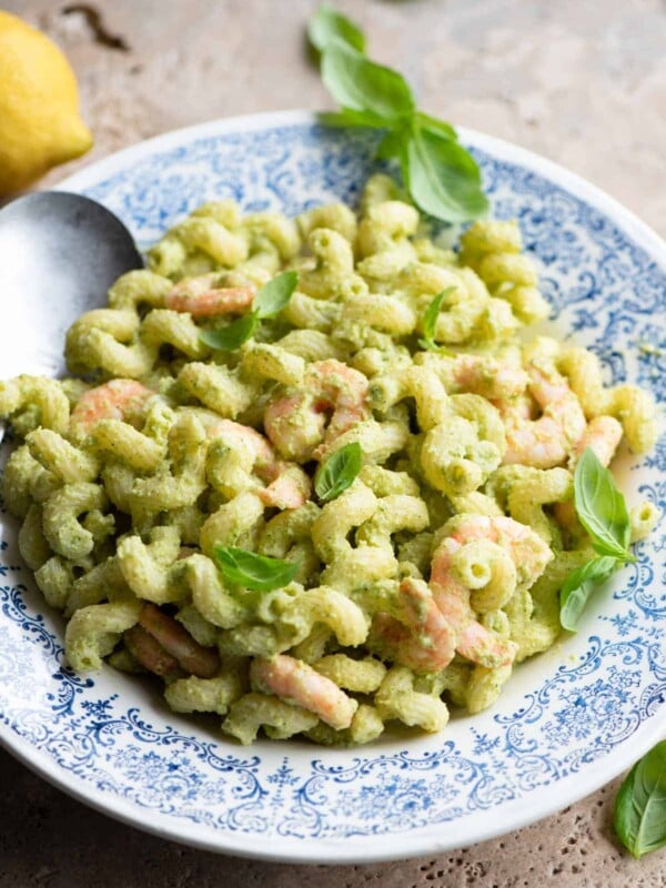 Zucchini shrimp pasta salad in a blue and white bowl topped with basil leaves.