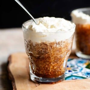 A cropped square image of a small glass filled with coffee granita and topped with whipped cream.