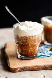 A small glass of coffee granita topped with whipped cream and a spoon in it.