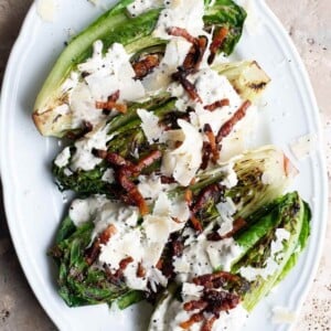 A close up of grilled romaine lettuce on a white plate topped with pancetta and Parmigiano Reggiano.