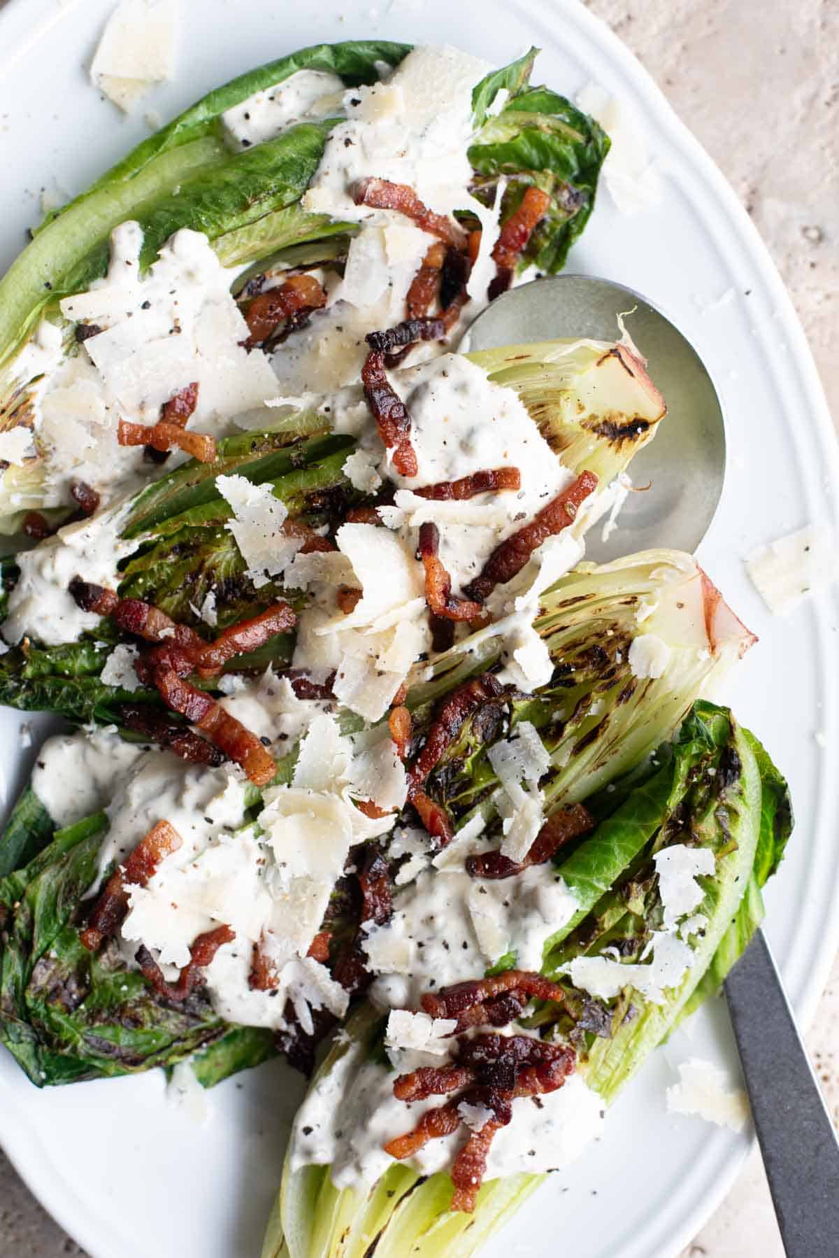 An overhead shot of grilled romaine lettuce topped with pancetta and a creamy dressing.