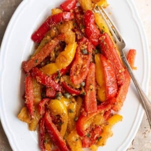 A cropped image of sauteed peppers mixed with capers and breadcrumbs on a white oval serving plate.