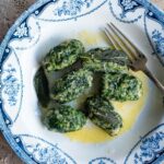 An overhead cropped image of Italian spinach and bread dumplings in a blue and white bowl with a butter sauce.