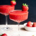 A close up of a frozen strawberry cocktail in a glass garnished with a whole strawberry.