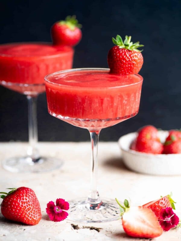 A side shot of a frozen strawberry cocktail in a glass garnished with a strawberry, the background is black.